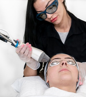 female med spa professional in protective glasses using laser skin treatment on female patient’s face